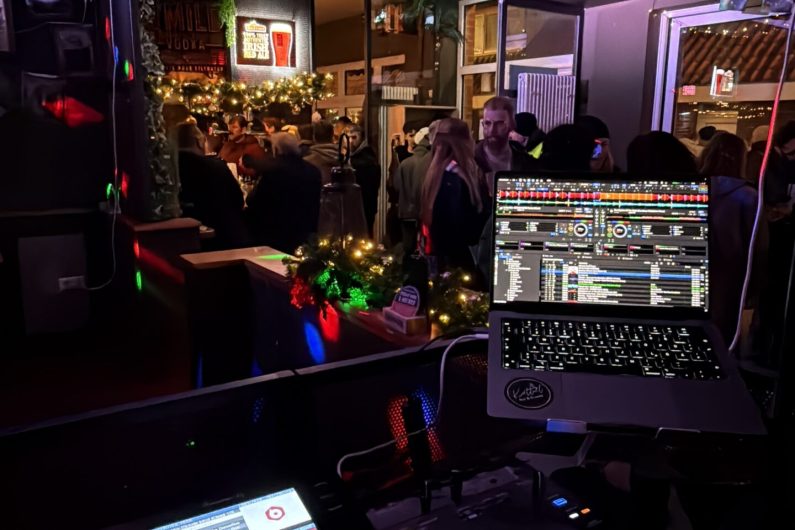 Feiernde Menschen in einer Bar, DJ Pult im Vordergrund
