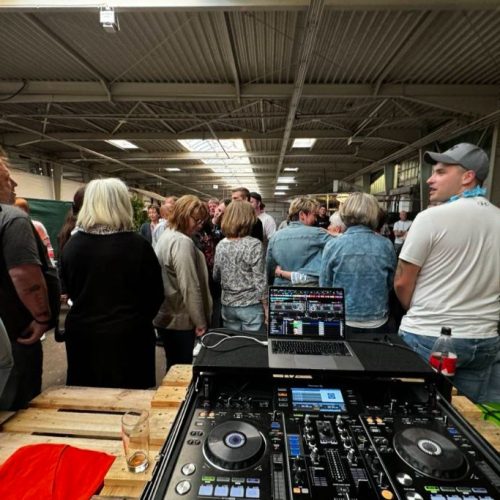 Menschen stehen um eine Tanzfläche herum, im Vordergrund das DJ Pult